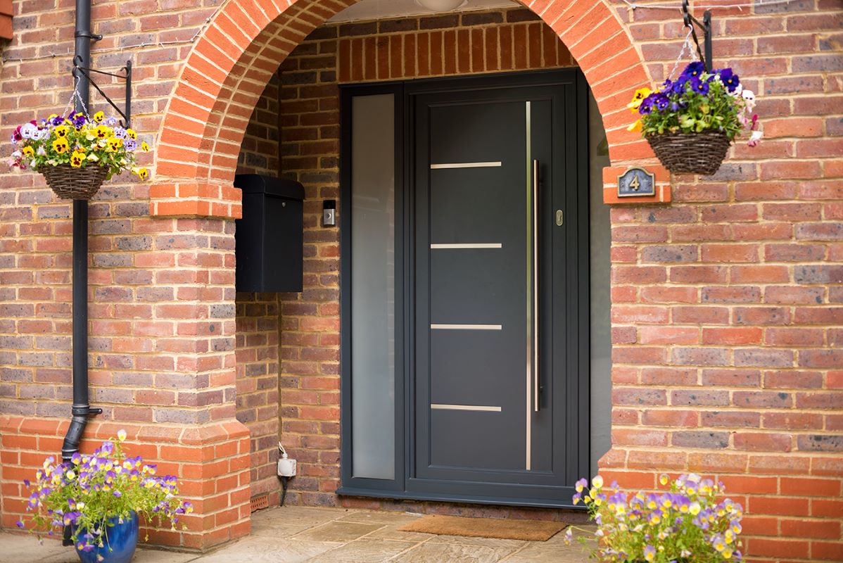 black origin aluminium entrance door, inside a red brick porch area with hanging baskets either side